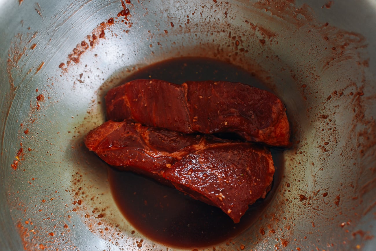 pork shoulder pieces in metal bowl with marinade