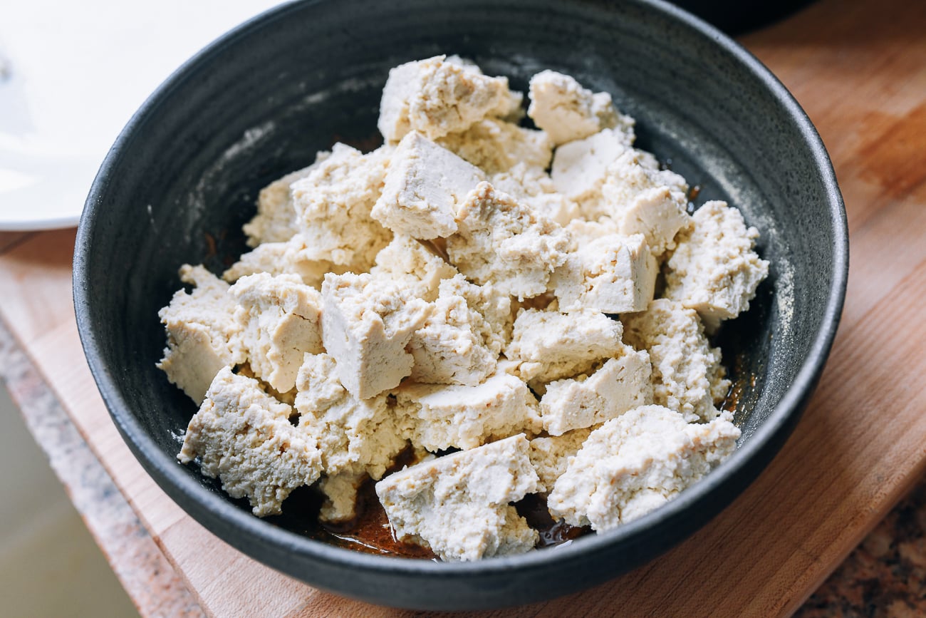 tofu torn into pieces in bowl of seasoning mixture