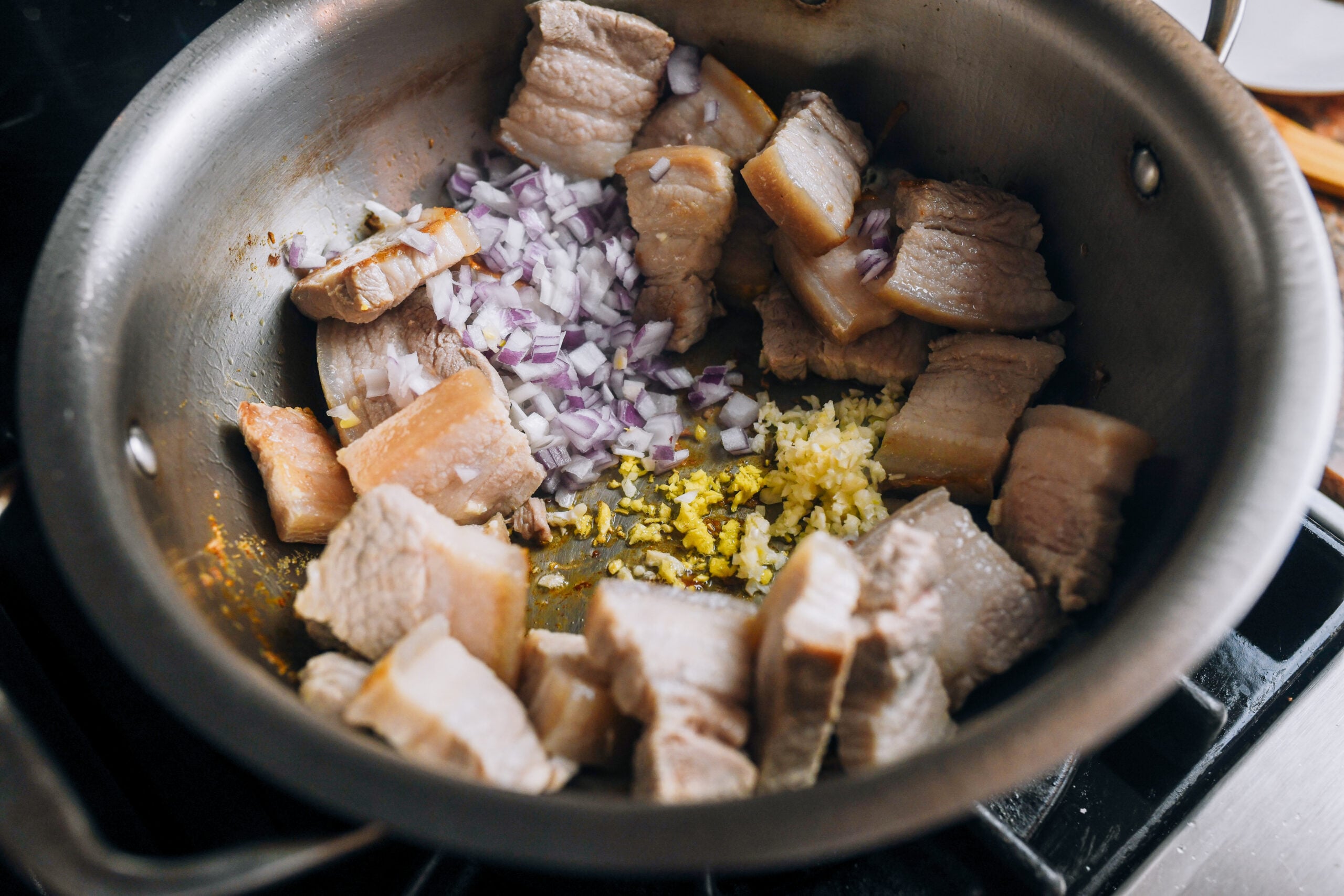 adding onion, ginger, and garlic to pork belly in pot