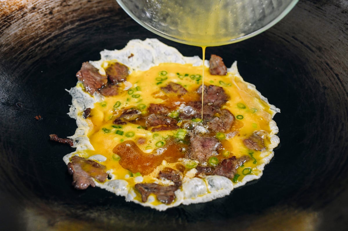 pouring scrambled eggs into wok with beef