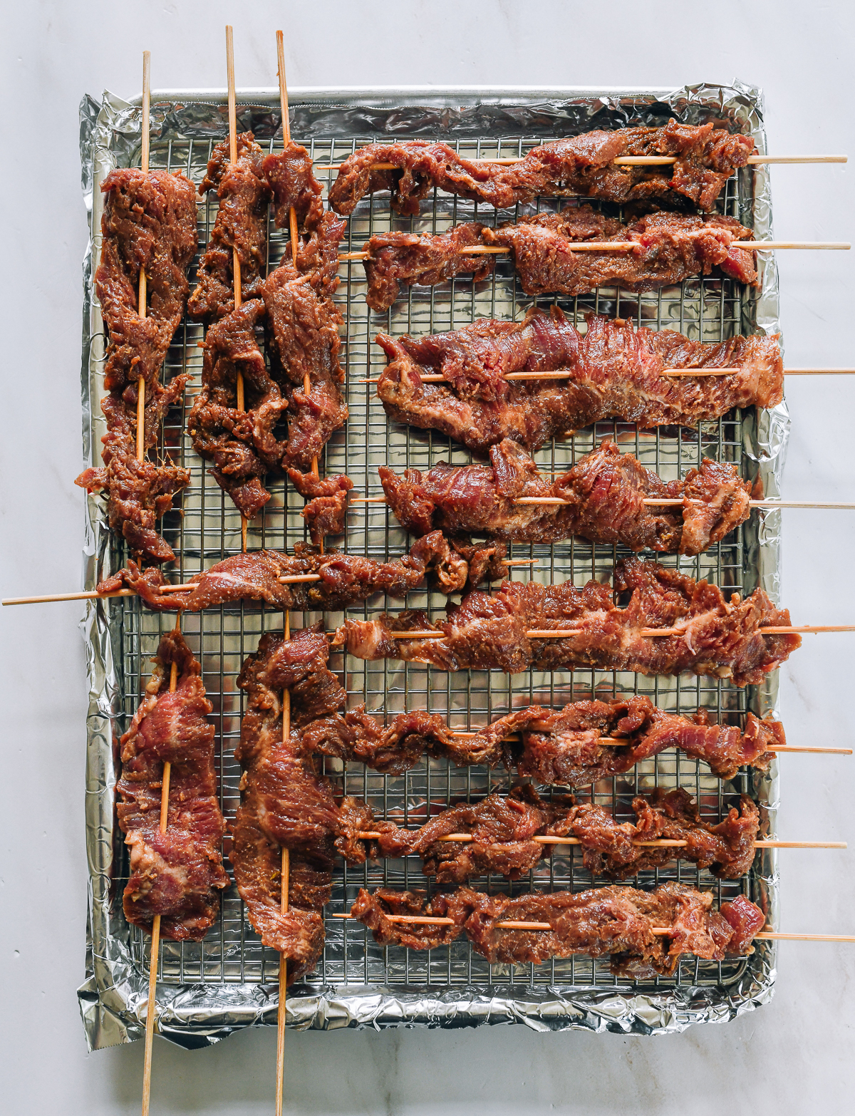 beef skewers laid out on wire rack on baking sheet