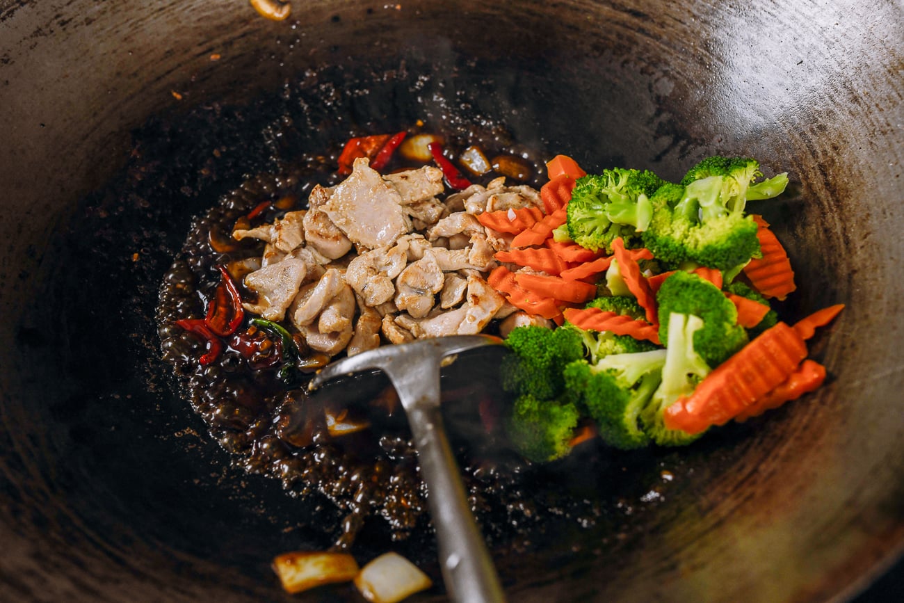 adding chicken and blanched broccoli and carrots back to wok