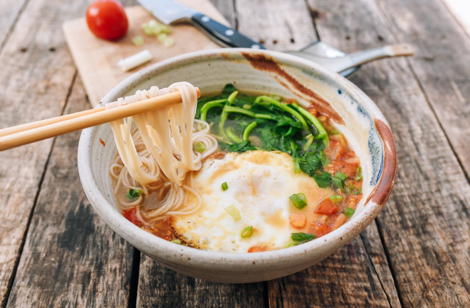 bowl of chinese noodle soup with tomato, egg, watercress