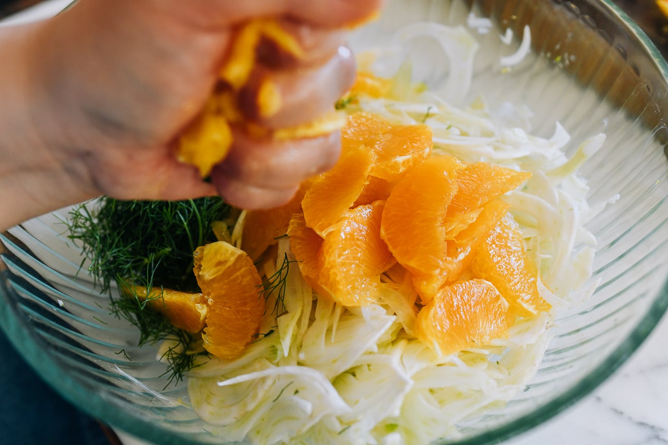 squeezing orange juice into bowl of fennel and orange salad