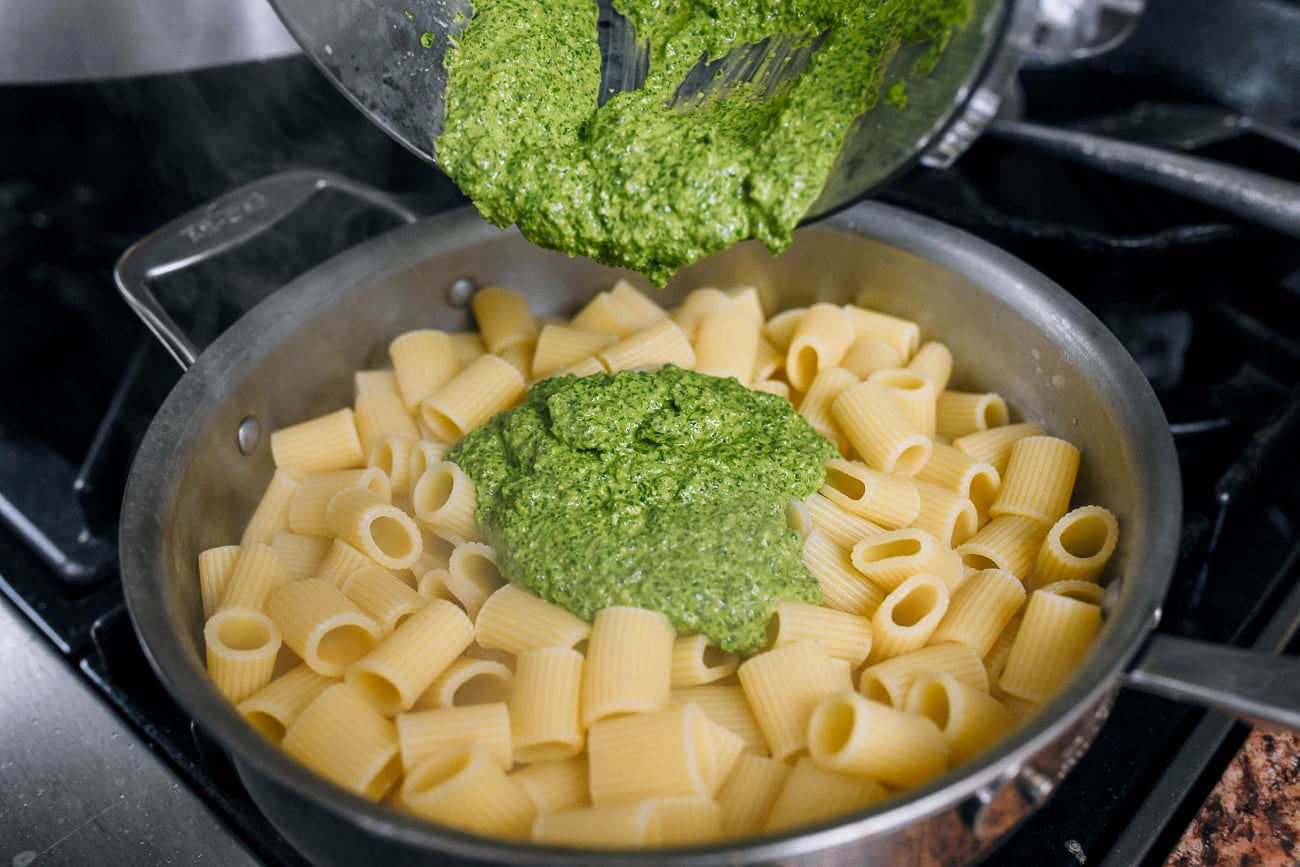 adding pesto to rigatoni in skillet
