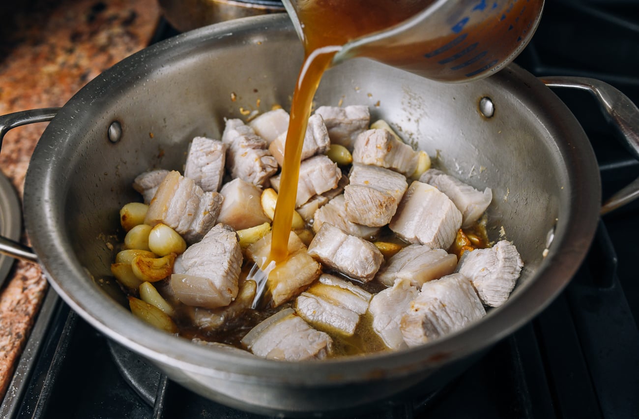 adding chicken stock and seasoning to pork belly in pot