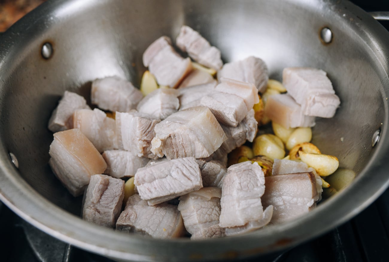 blanched pork belly pieces in pot with garlic cloves