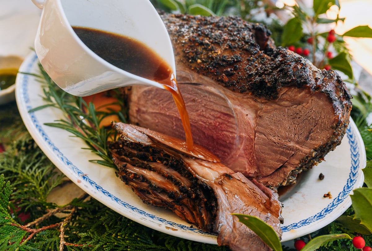 pouring jus on top of roast lamb slices
