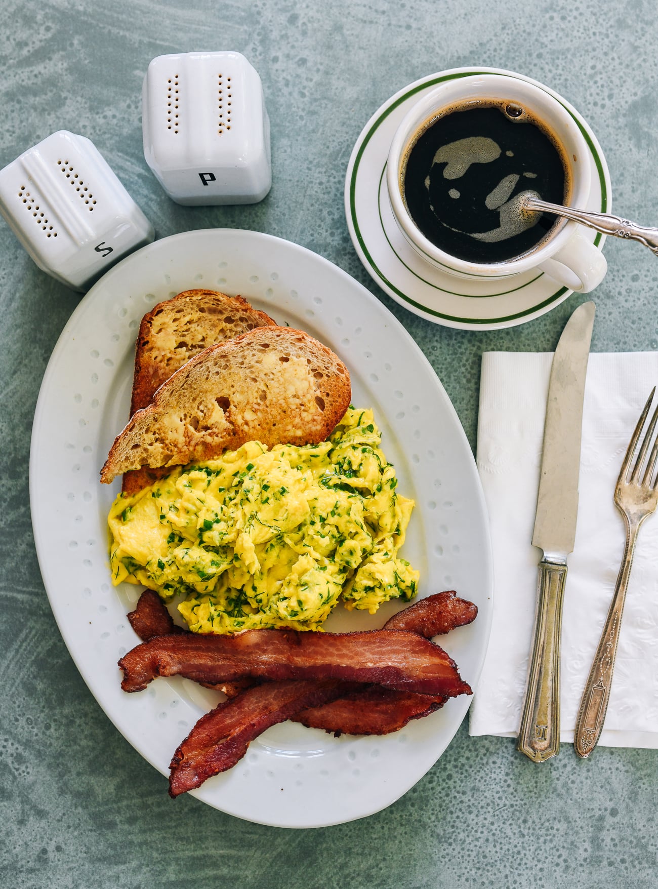 herby scrambled eggs with toast, bacon, and coffee