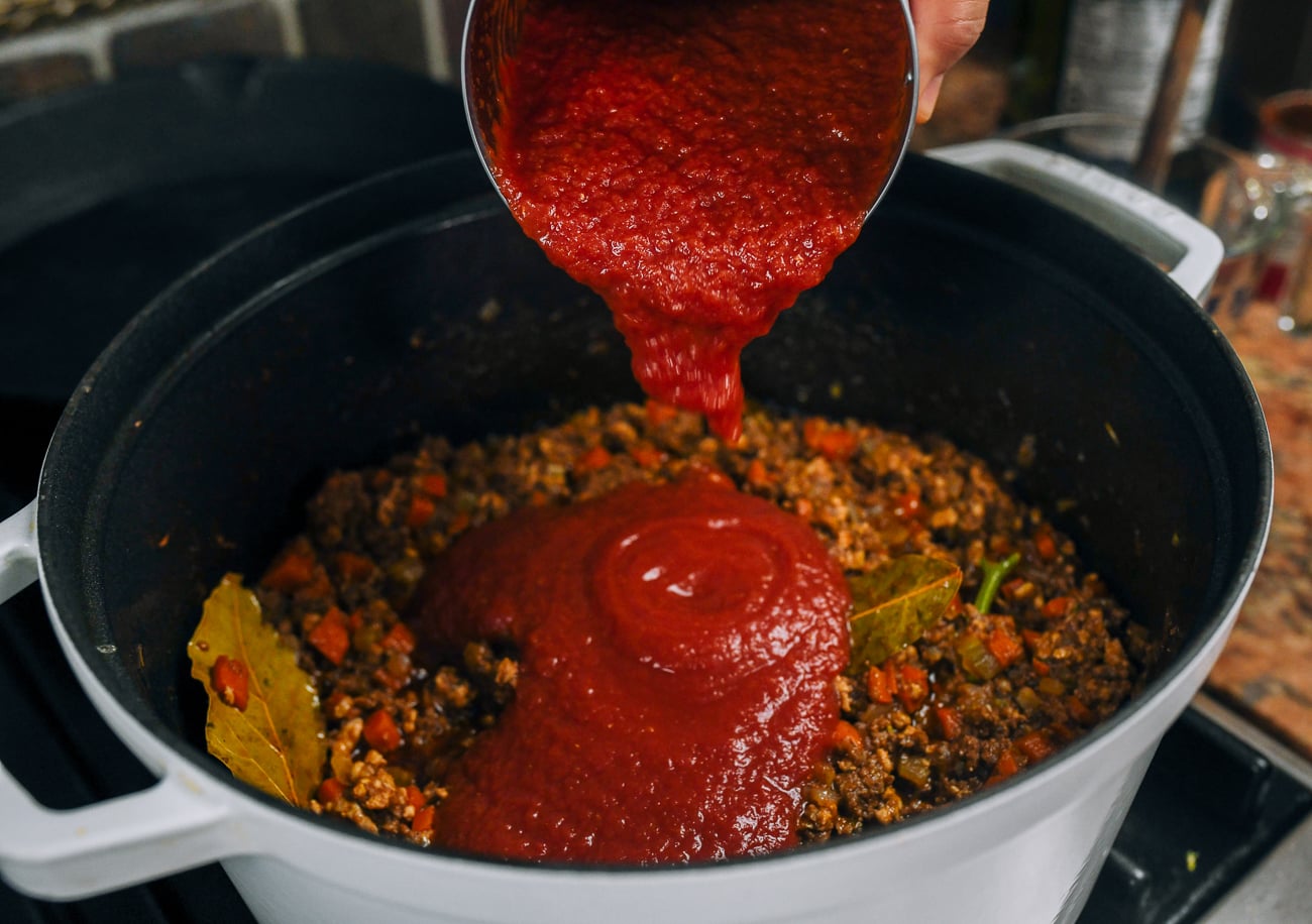adding tomato puree to meat sauce
