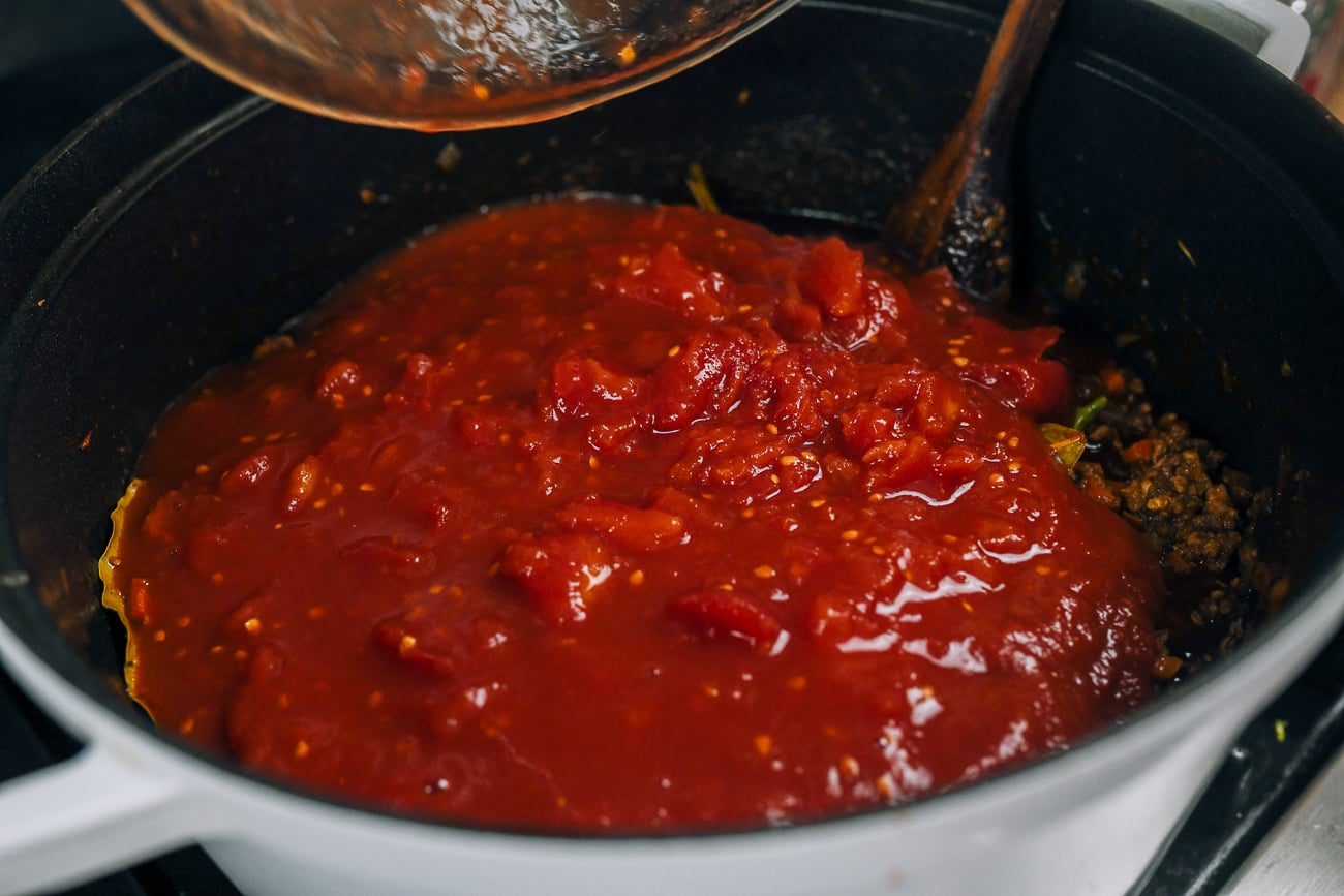 adding tomato chunks to meat sauce
