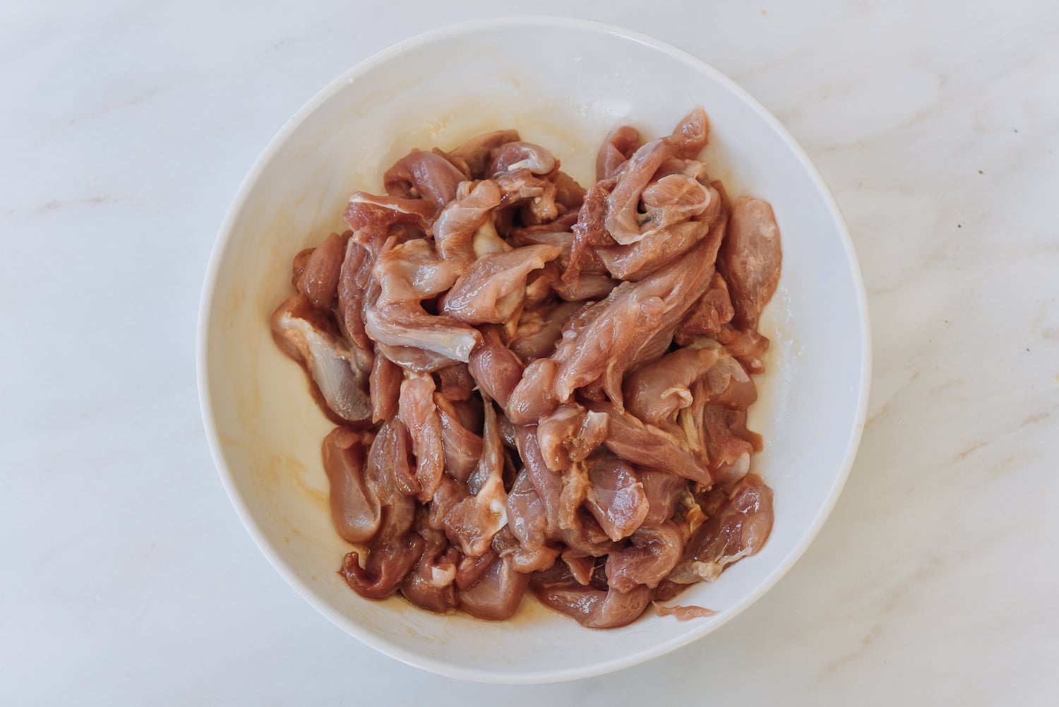 marinated strips of  boneless skinless chicken thigh in white dish