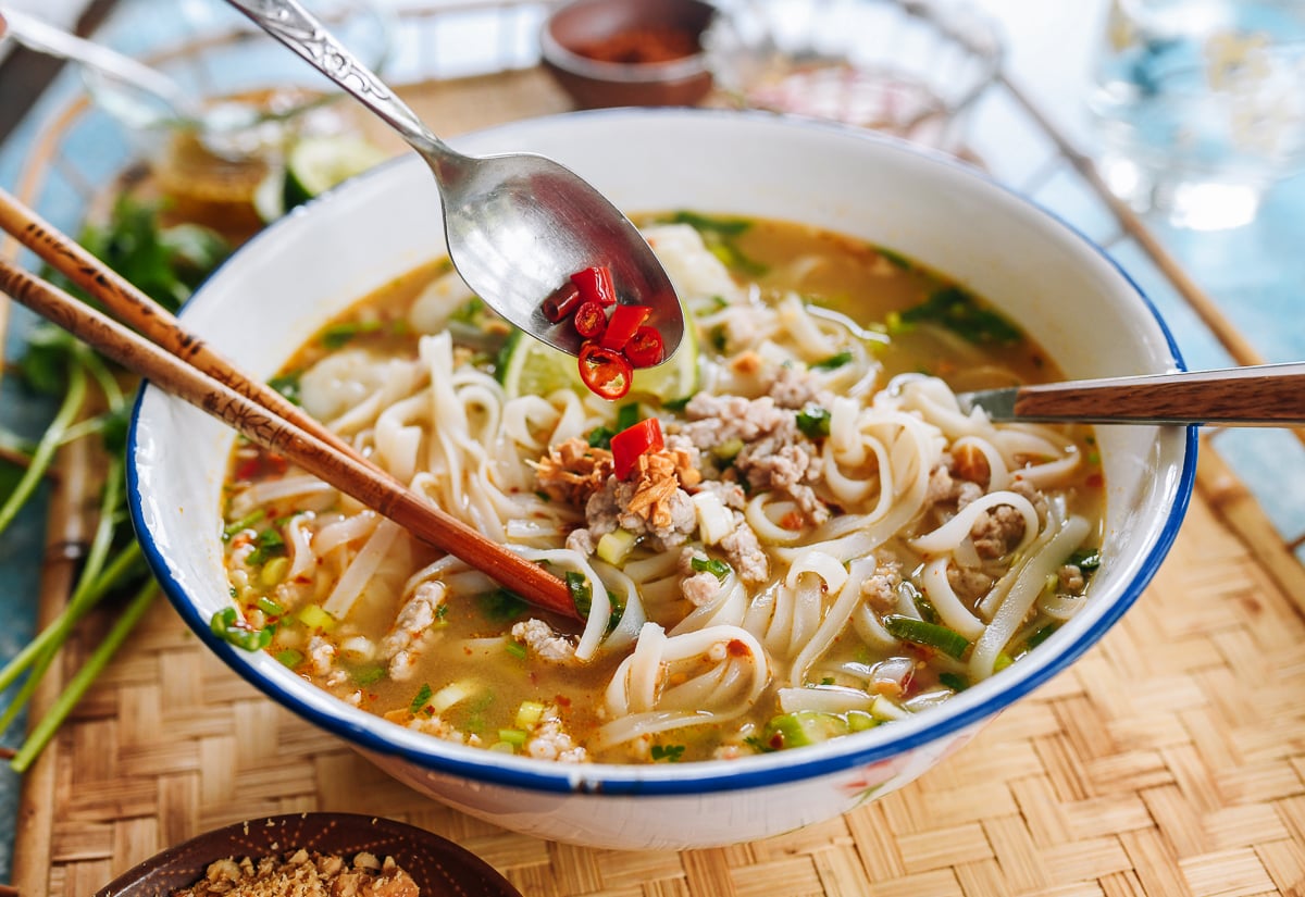 pouring chili vinegar over tom yum noodle soup