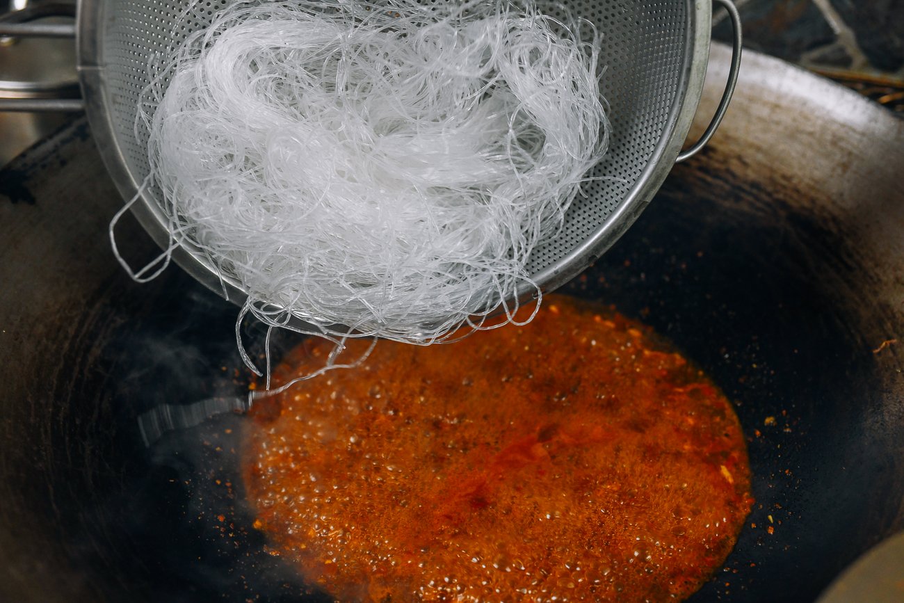 adding glass noodles to liquid in wok